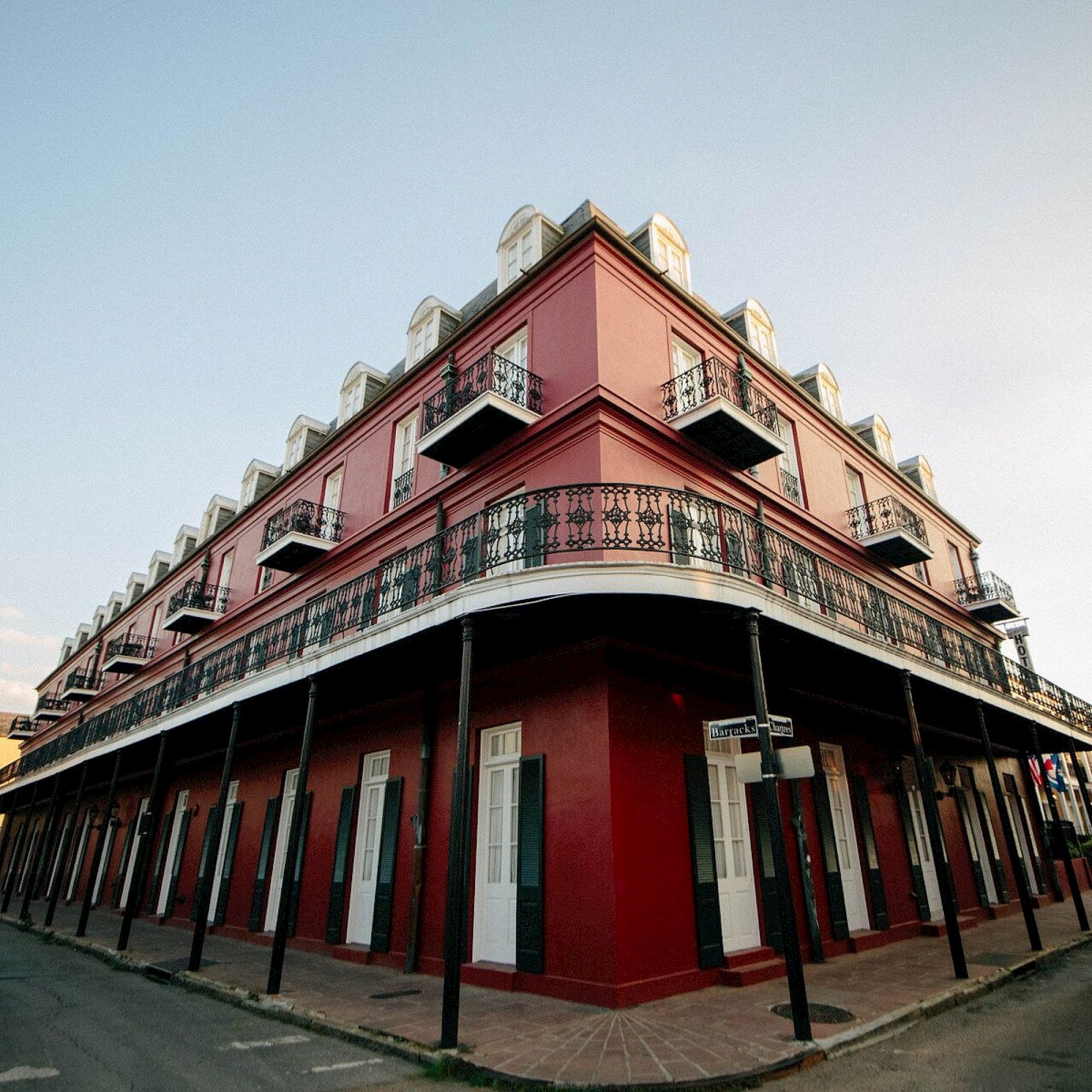 A corner red building with white windows and a wrought iron balcony, set against a blue sky, located in a seemingly historic area.