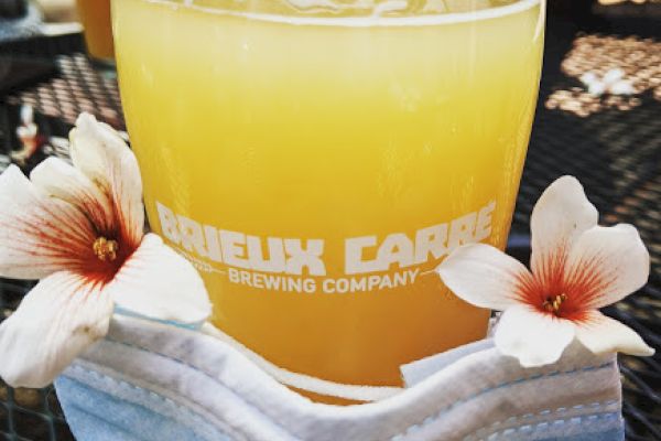 A glass of orange beer with a brewery logo, decorated with flowers and placed on a face mask.