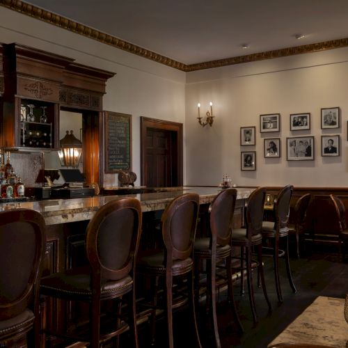 This image shows a dimly lit bar with classic wooden stools, a marble counter, and framed photos on the wall, creating a cozy atmosphere.