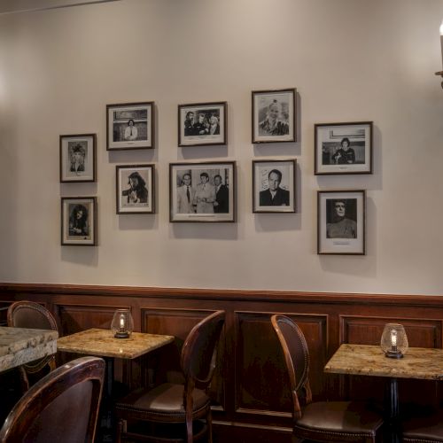 A cozy cafe interior with framed photos on the wall, tables, chairs, candlelights, ornate wall sconces, and a marble counter.