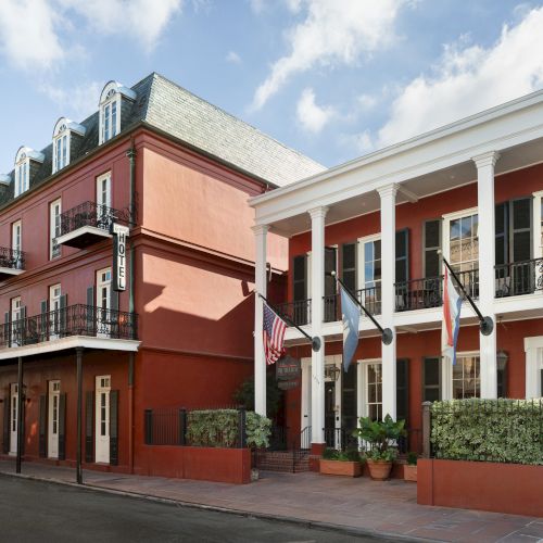 A red historic-style building with balconies and several flags displayed in front, under a blue sky with clouds.