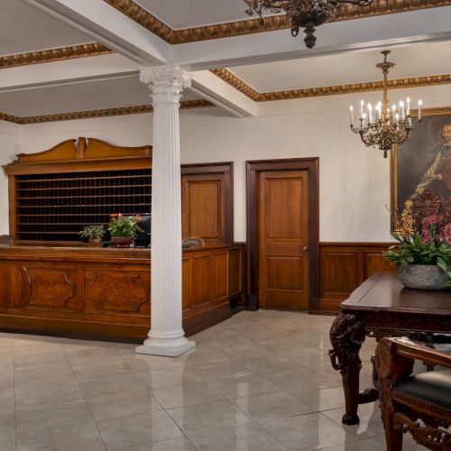 This image shows a classic hotel reception area with wooden furnishings and a large portrait on the wall.