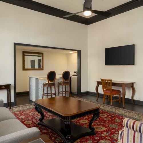 The image shows a living room with a sofa, chairs, a coffee table, and a TV. There's also a small bar area with stools.