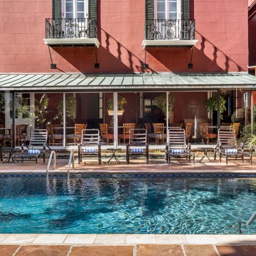 A swimming pool with lounge chairs is set in front of a red building with balconies and large windows.