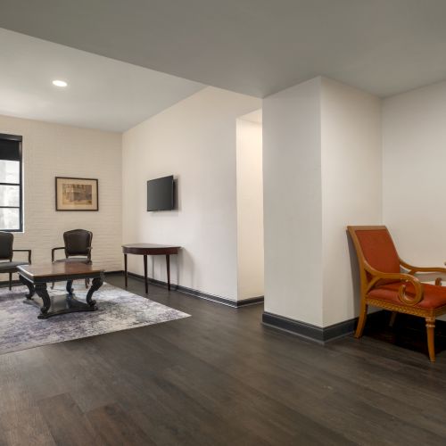 A spacious room with seating furniture, a TV, and a small table with chairs; modern, minimalistic design in neutral tones.