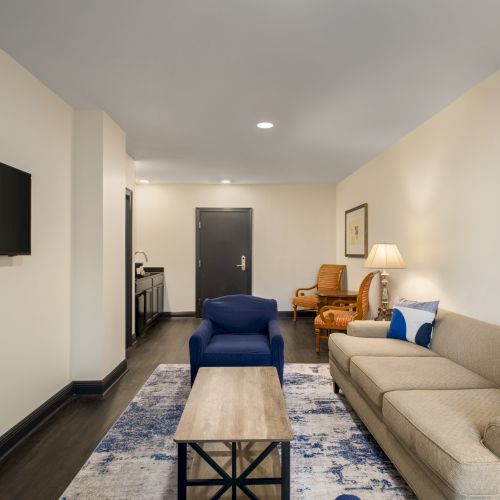 A modern living room with a beige sofa, blue accents, a wall-mounted TV, art, and a coffee table on a patterned rug.