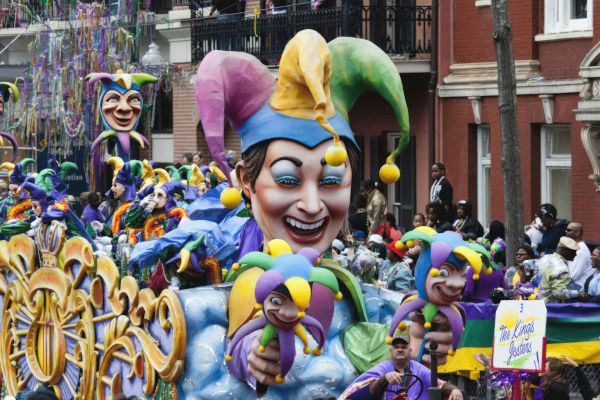 A lively parade with colorful floats, jester figures, and people dressed in costumes, creating a festive atmosphere.