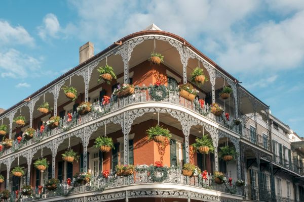 A historic building with ornate ironwork balconies and hanging plants under a blue sky with scattered clouds.