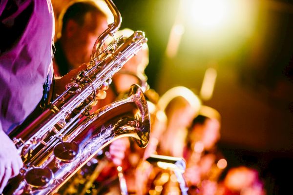 A group of musicians playing saxophones, captured under vibrant stage lighting, creates a lively and warm atmosphere.