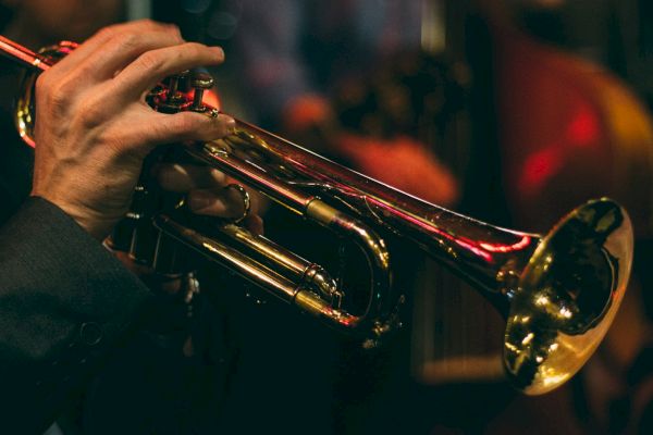 A person is playing a brass trumpet, captured in a dimly lit setting, likely at a live music performance or jazz club.