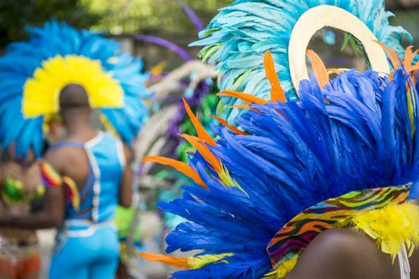 People are wearing vibrant costumes with colorful feathered headdresses, possibly at a parade or festival.